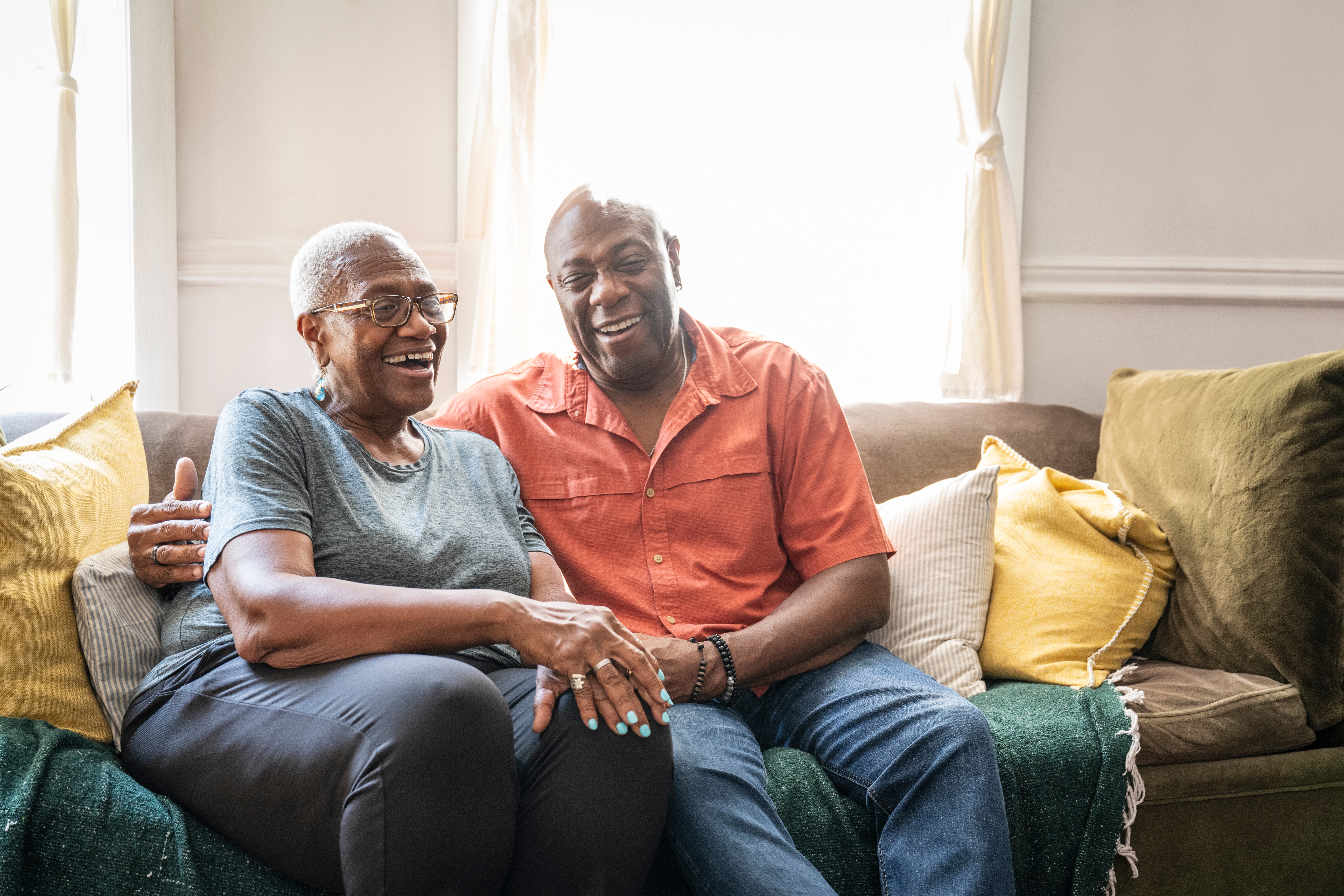 Older couple sitting on a couch at home, smiling and embracing, conveying warmth and affection