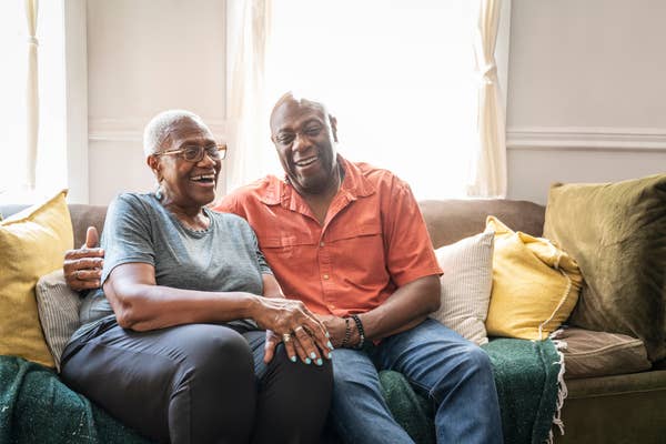Older couple sitting on a couch at home, smiling and embracing, conveying warmth and affection
