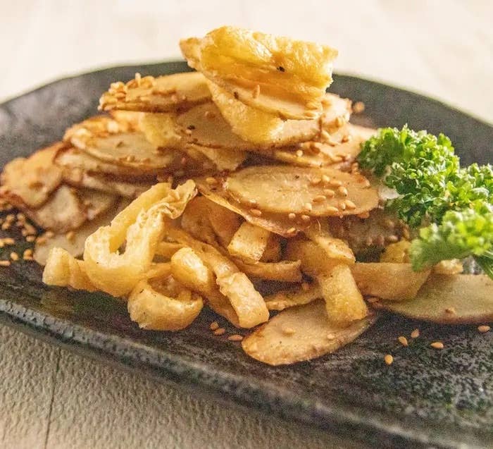揚げごぼうのスライスが盛られた黒い皿に盛られ、ゴマとパセリが添えられた料理。