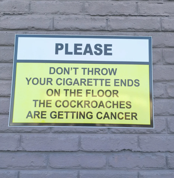 Sign connected  a ceramic  partition  humorously urges not to litter cigaret  ends, suggesting cockroaches are getting cancer