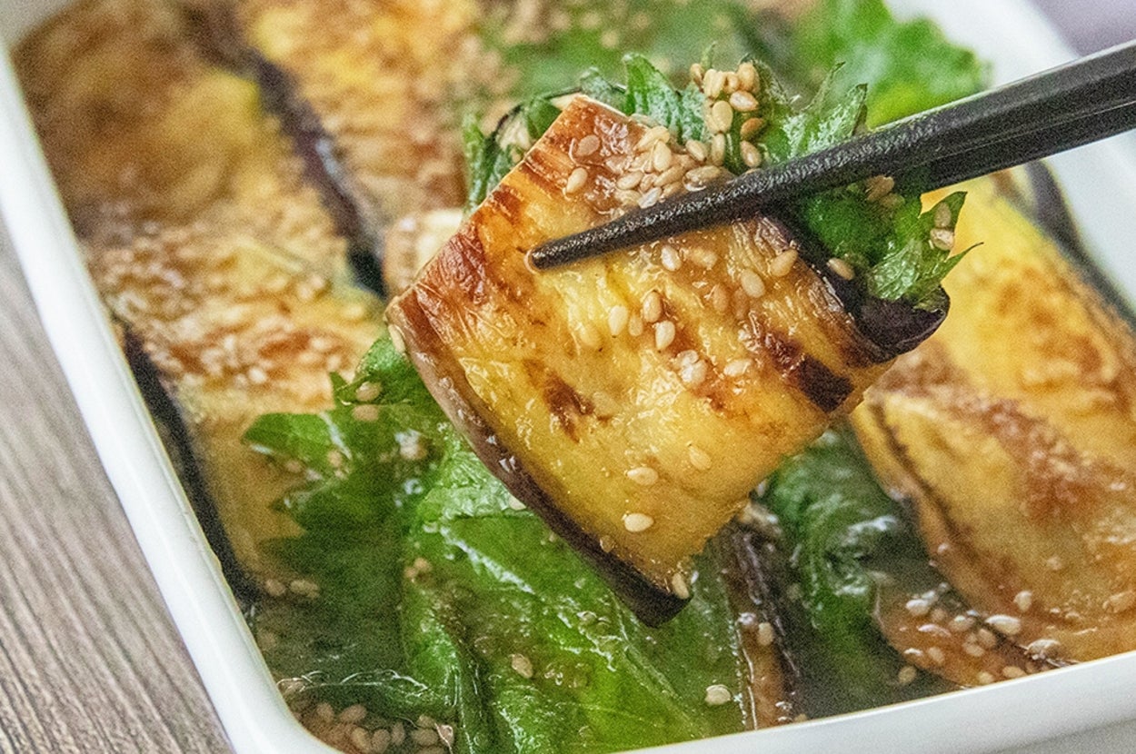 たれがかかった焼きなすと大葉が箸で持ち上げられている。
