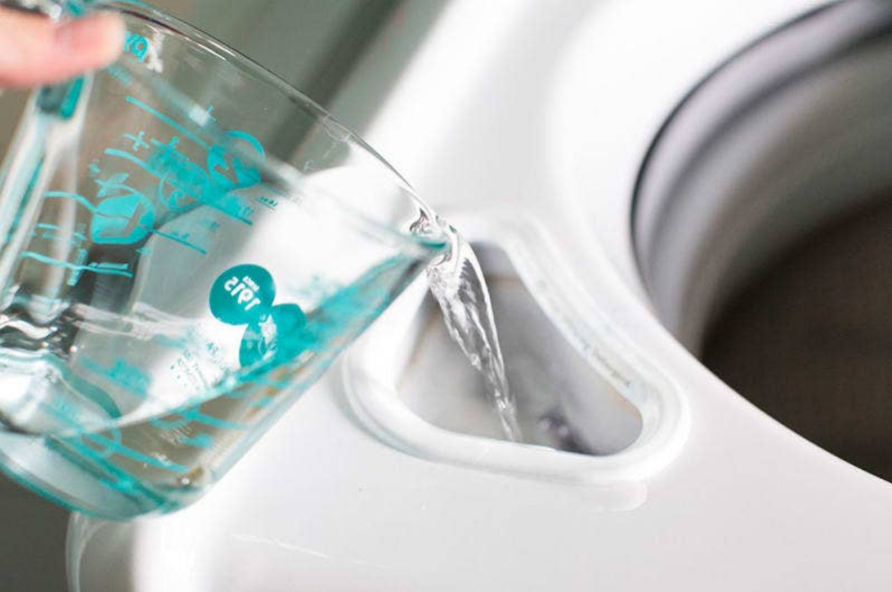 Pouring water from a measuring cup into a washing machine detergent compartment