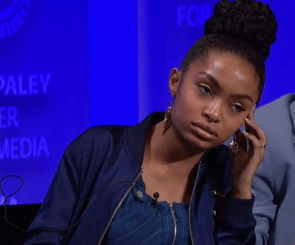 Person listening attentively during a panel discussion, wearing a stylish jacket and hoop earrings
