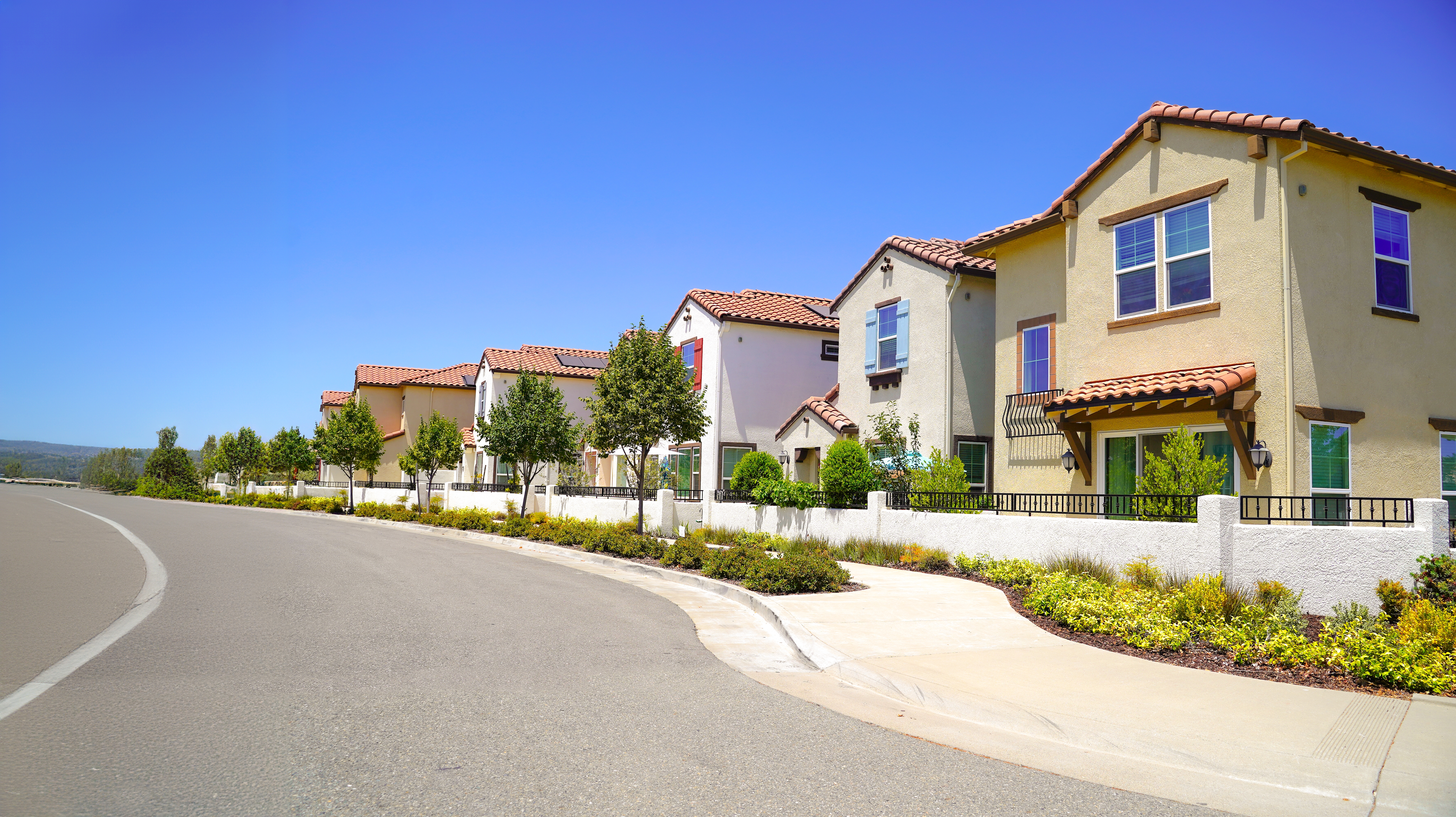 En rad med moderne forstadshus med flislagte tak og godt vedlikeholdte hager, foret langs en rolig gate under en klar himmel