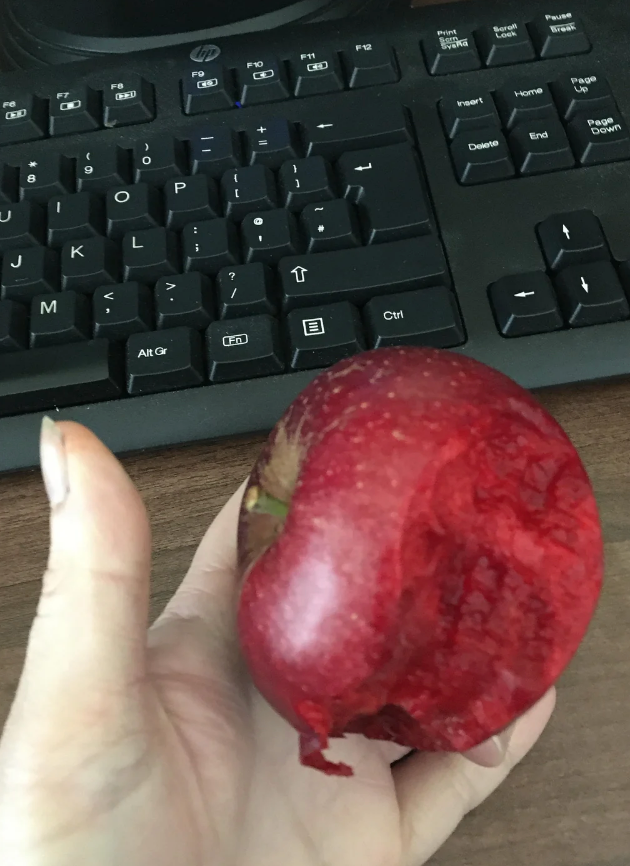 A manus holding a reddish pome with a ample wound taken out, successful beforehand of a keyboard