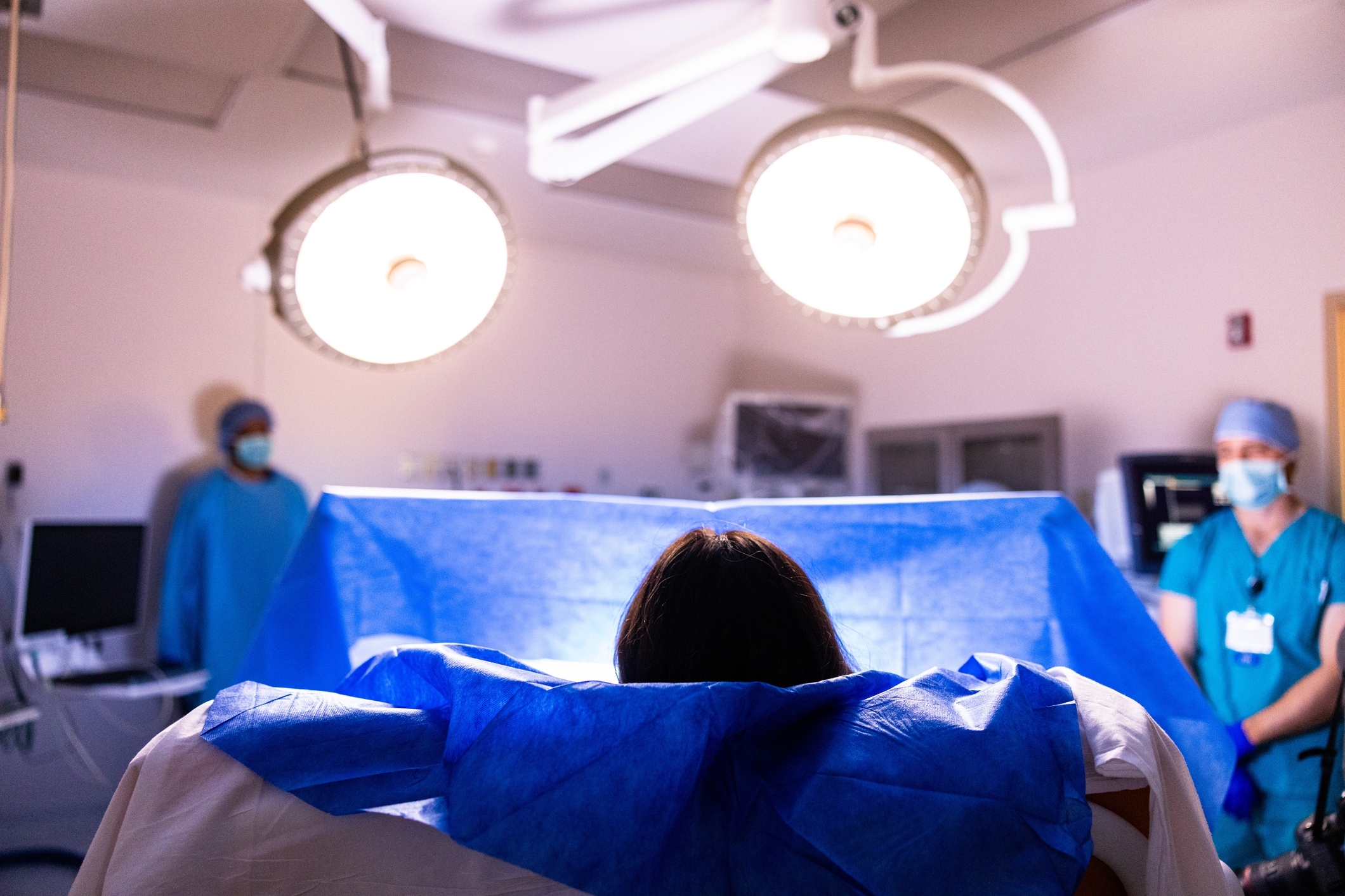 Medisinske fagpersoner i kirurgisk antrekk står i nærheten av en pasient i et operasjonsrom med lyse overheadlys