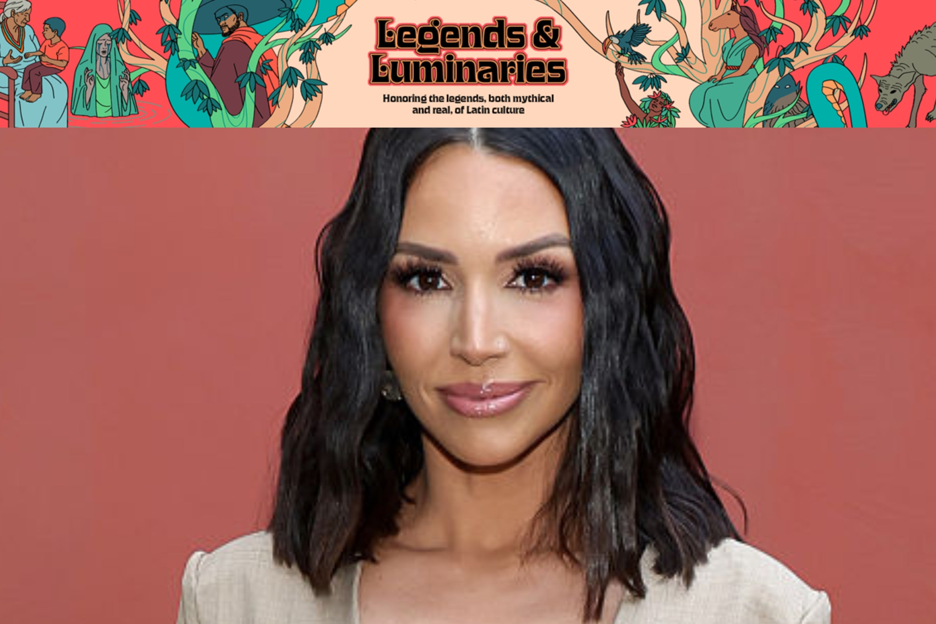 Celebrity with wavy shoulder-length hair smiles on a red carpet, wearing a sleeveless dress. Background features "Legends & Luminaries" text