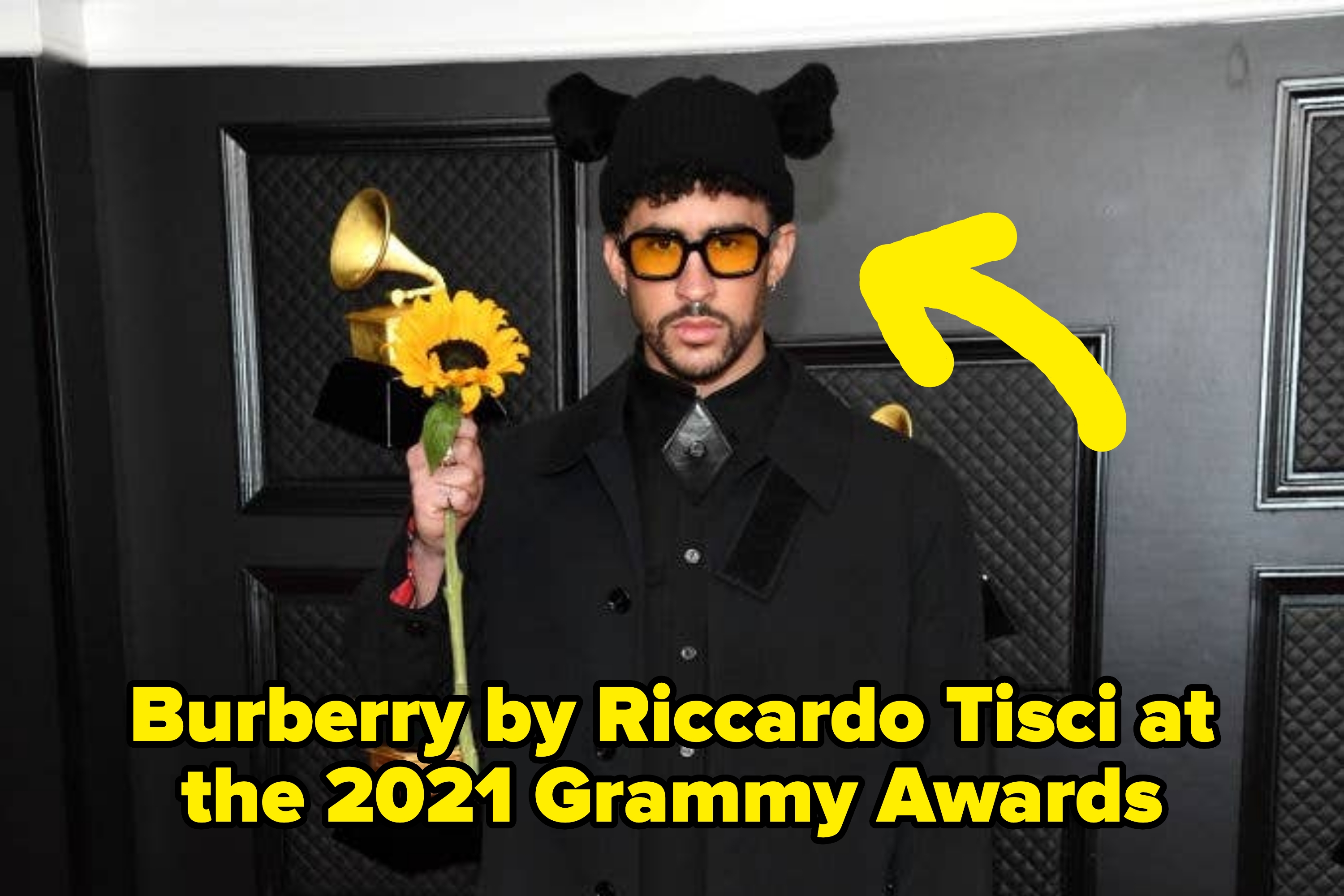 Person in avant-garde outfit holds sunflower in front of Grammy awards backdrop