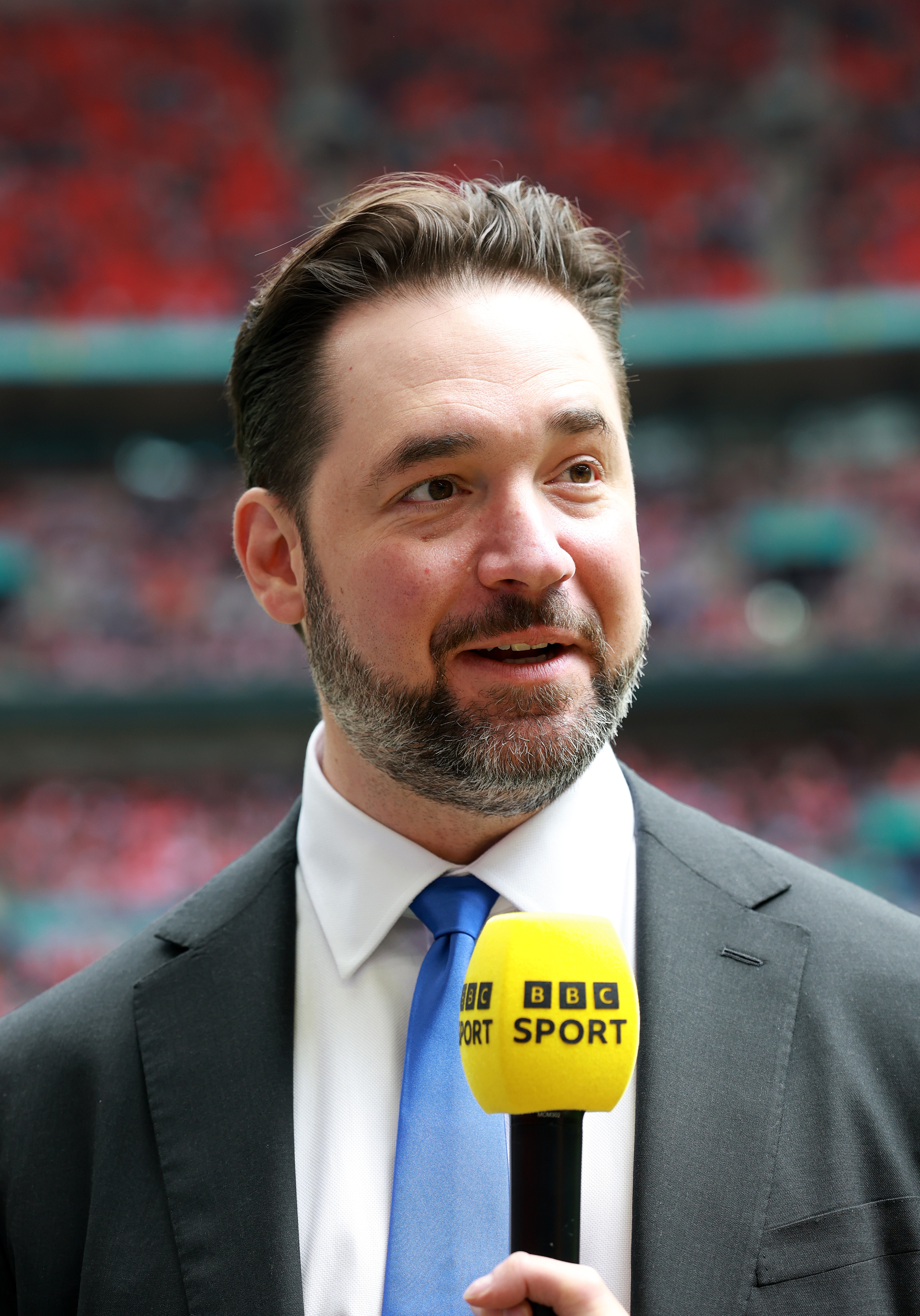 Alexis Ohanian in a suit holds a BBC Sport microphone while speaking