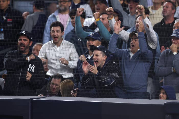 Excited crowd at a baseball game cheering behind a protective net, featuring fans in Yankees apparel