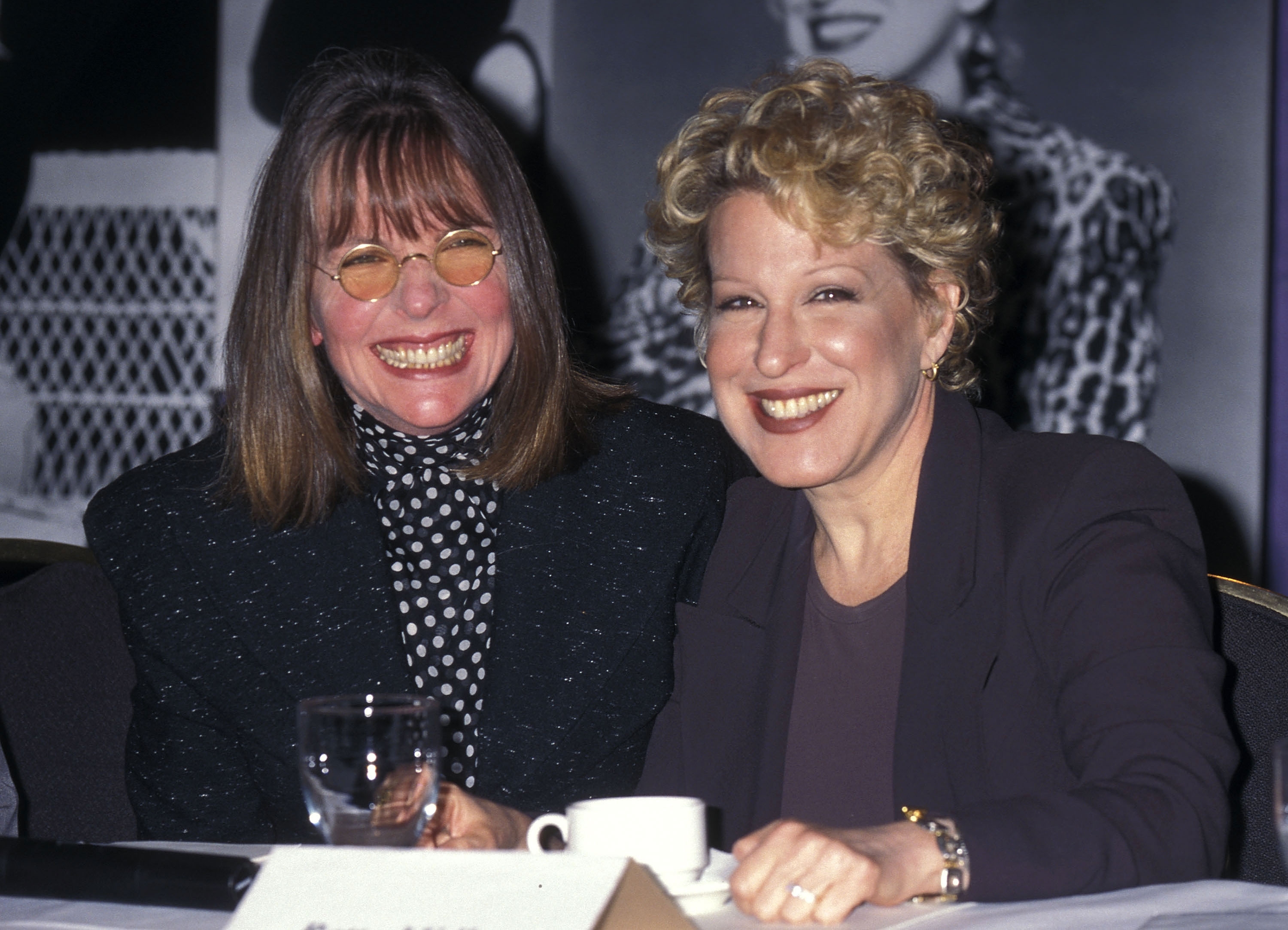 Diane Keaton and Bette Midler are sitting together, smiling at a formal event