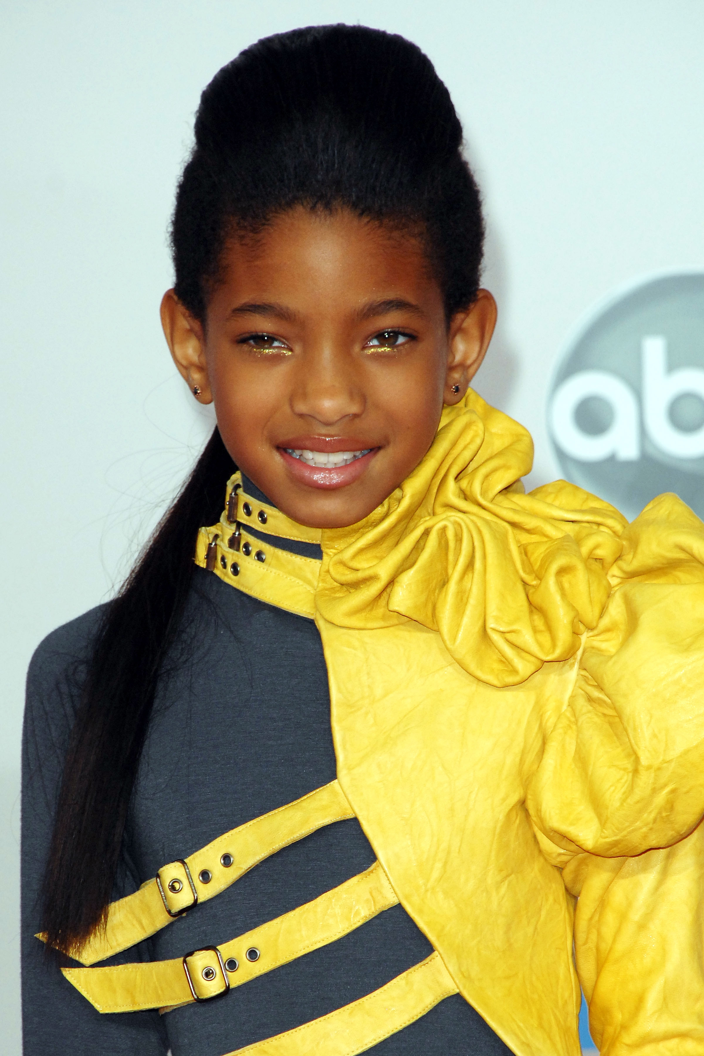 Willow Smith in a stylish outfit with a high collar and unique shoulder design, smiling at an event