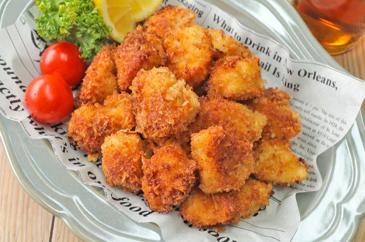 レモンとトマト、パセリを添えた揚げ物が紙の上に盛られている皿。お茶が横にある。