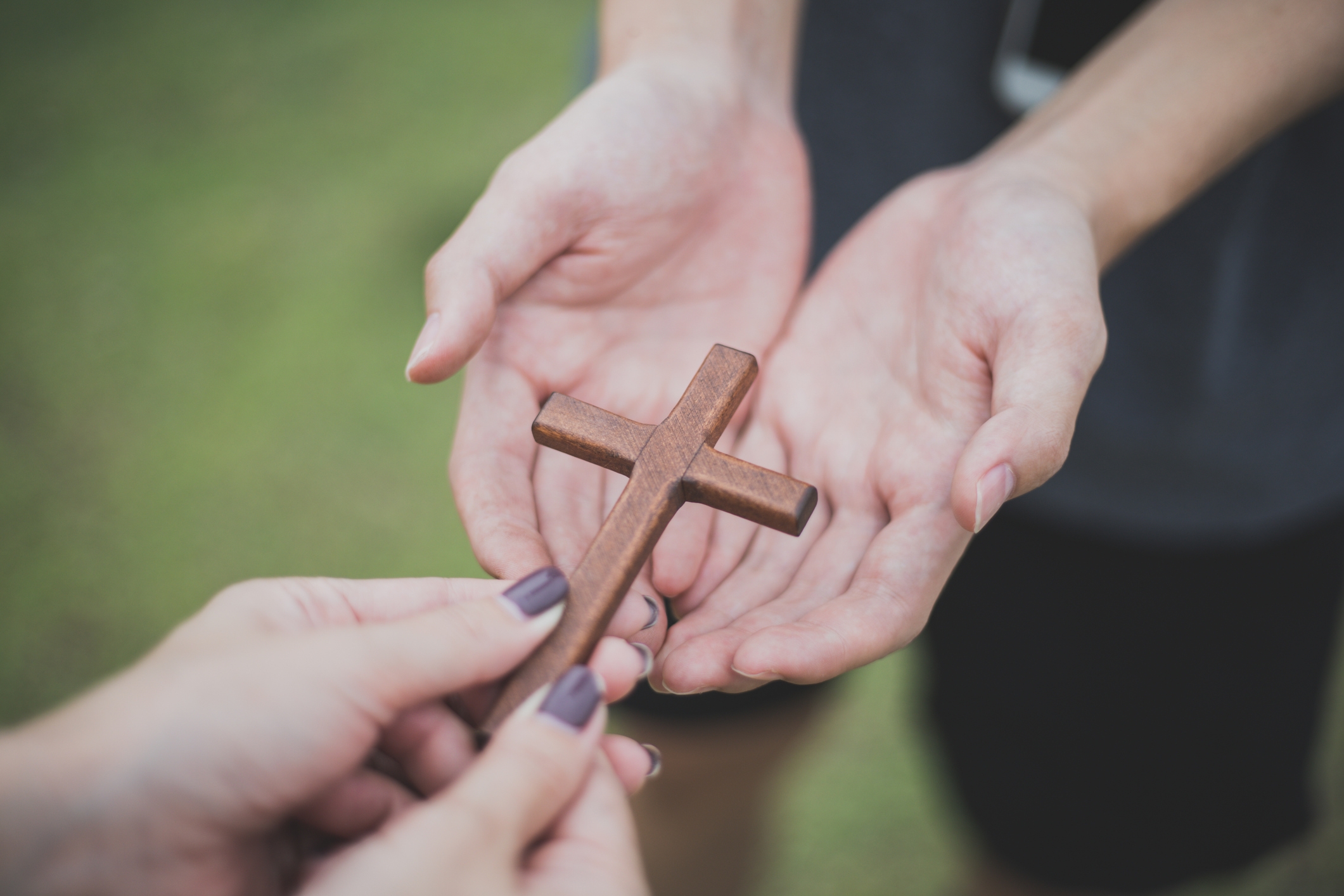 Hands exchange a small wooden cross