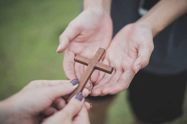 Hands exchange a small wooden cross