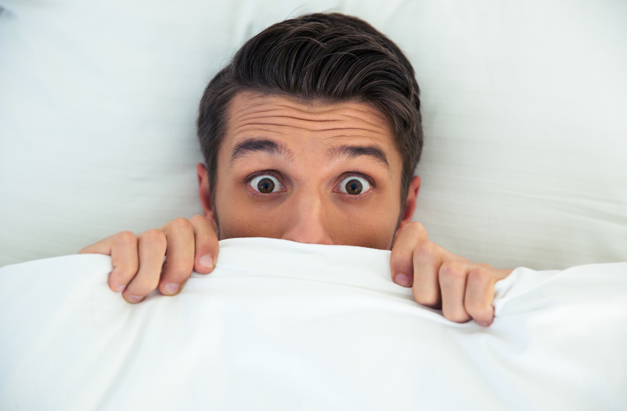 Person in bed, eyes wide open, peeking over covers, conveying surprise or anticipation