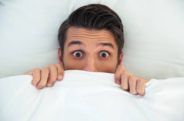 Person in bed, eyes wide open, peeking over covers, conveying surprise or anticipation