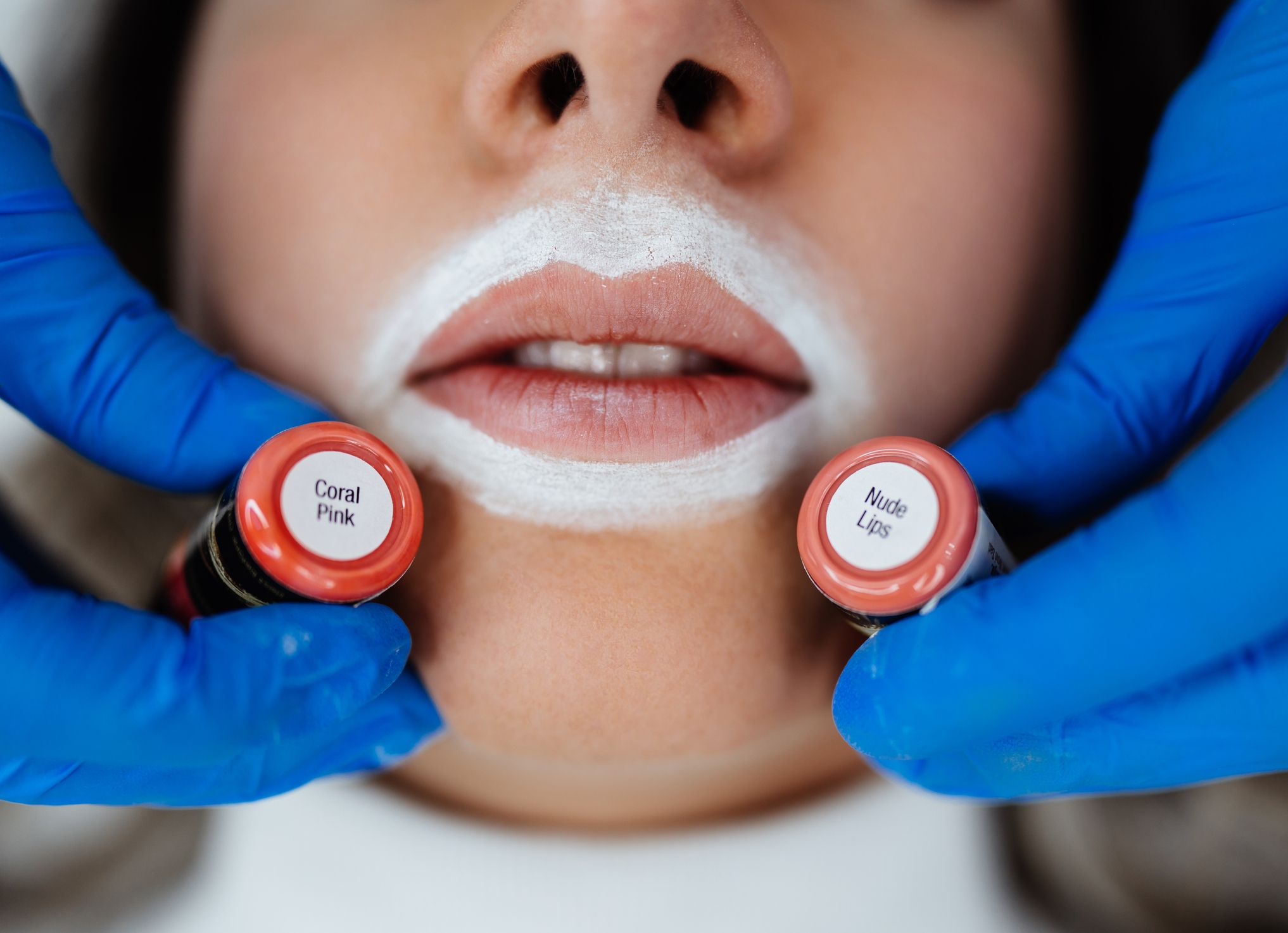 Person med hvit kontur rundt munnen holder to leppepigmentflasker merket 