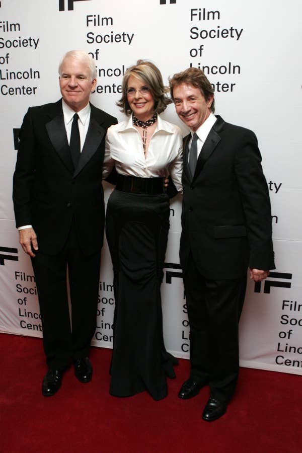 Three people on the red carpet at a Film Society event, in formal attire: two men in tuxedos and a woman in a stylish gown with a fitted waist