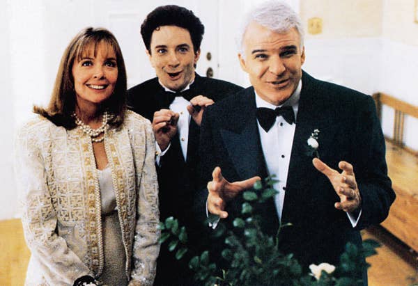 Three people pose indoors; a woman in an embellished jacket and two men in tuxedos with playful expressions