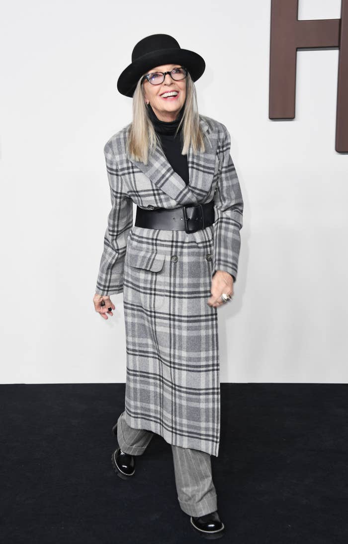 Person in a plaid coat, black hat, and belt at a celebrity event