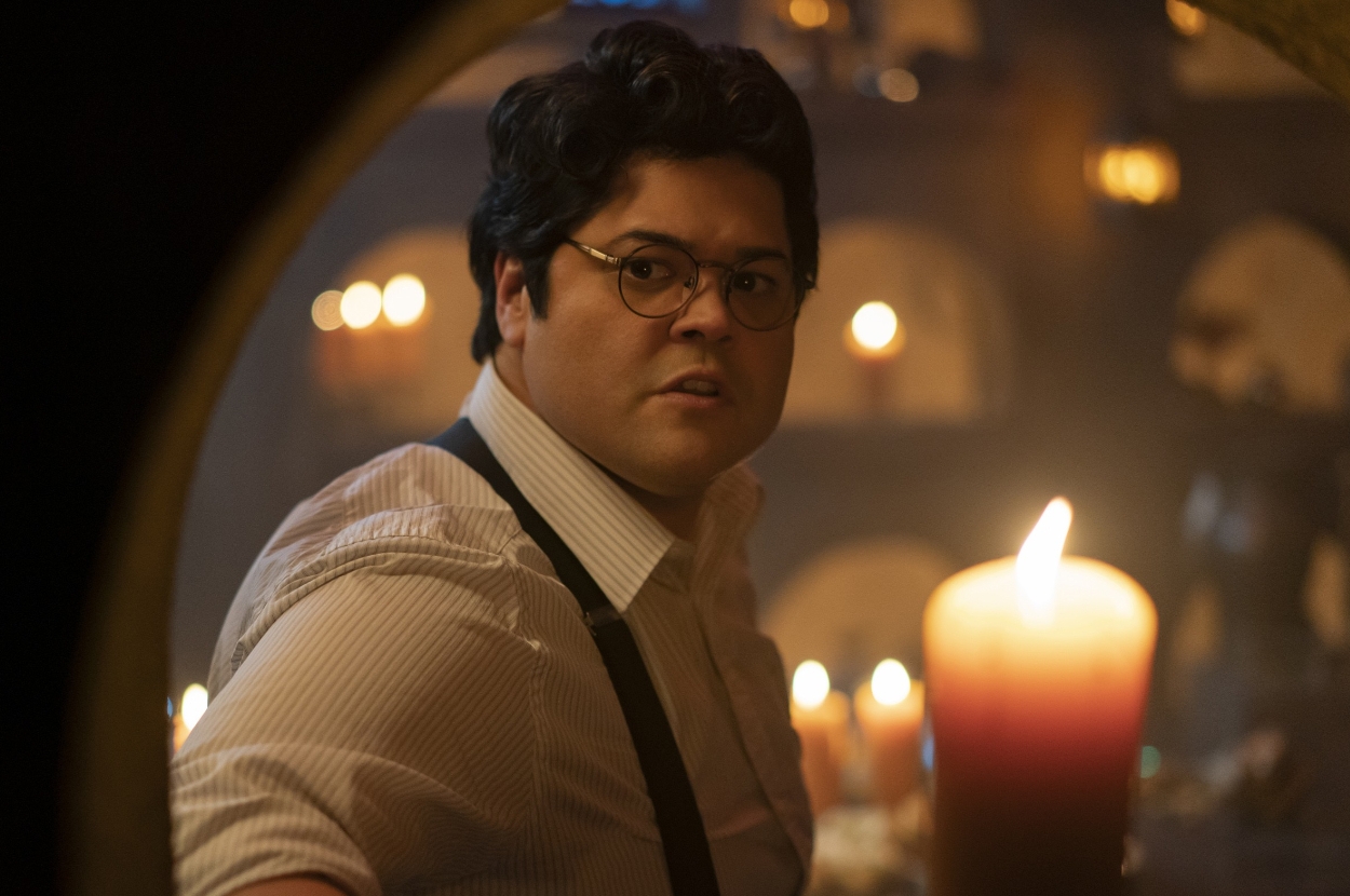 A person with glasses and a button-up shirt inside a dimly lit room with candles, looking concerned or startled