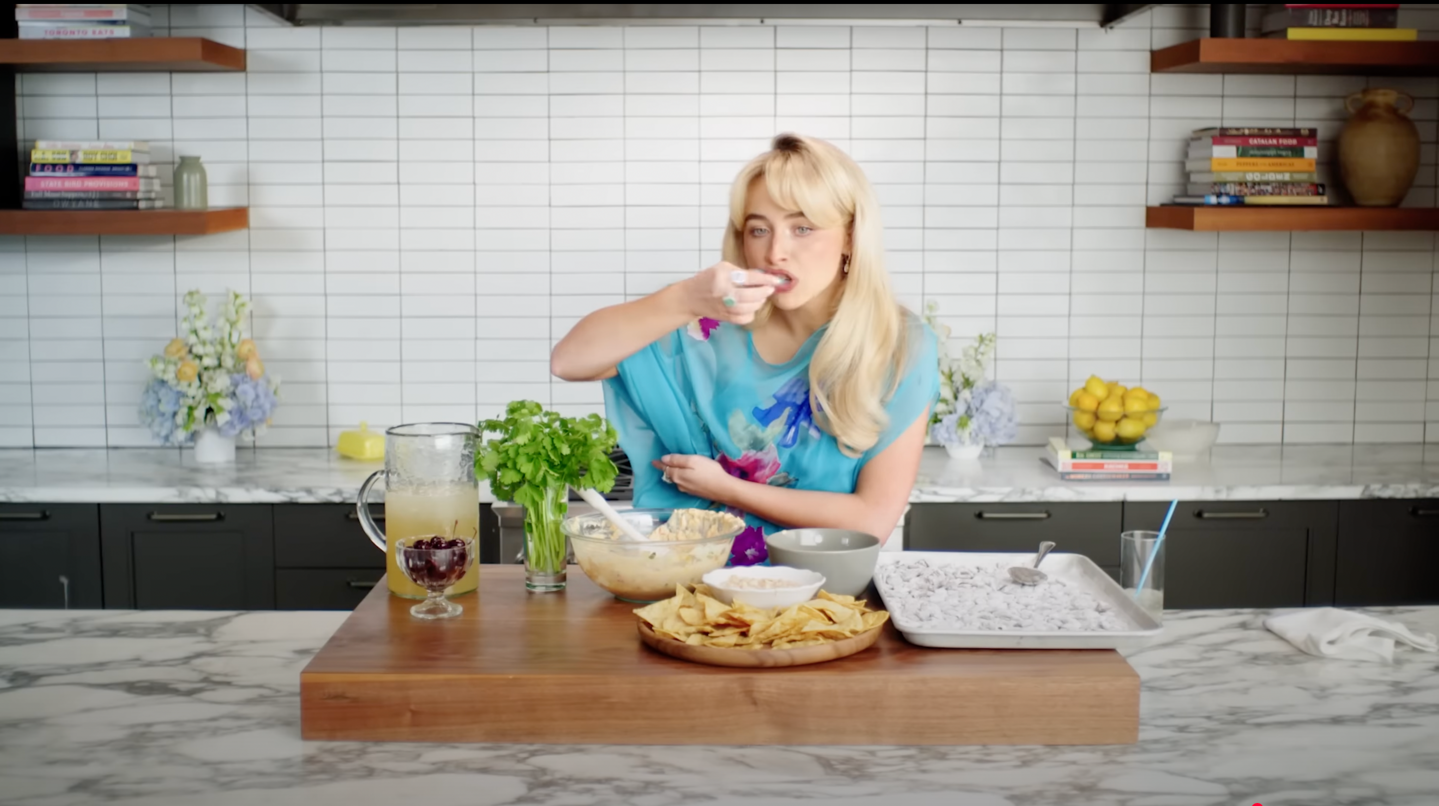 Person in a kitchen setting, enjoying a snack. Ingredients and prepared food items are spread on the table