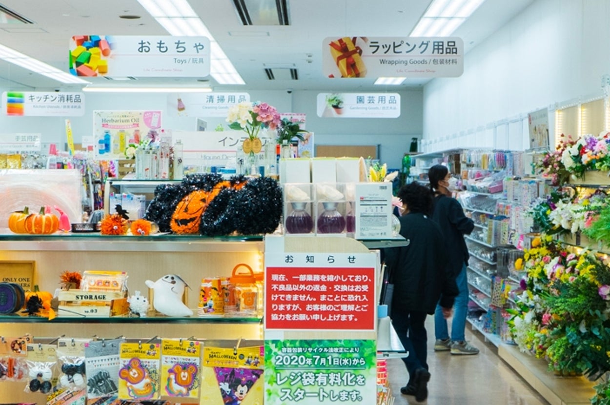 ダイソー店内のハロウィングッズ販売コーナーで、買い物をする人々の様子。フラワーアレンジメントも展示されています。