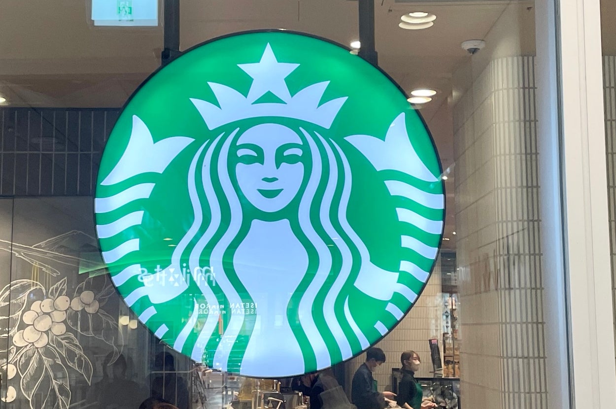スターバックスのロゴが窓に表示された店内のシーン。人々がカウンターでくつろいでいる。