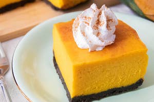 かぼちゃのチーズケーキにホイップクリームがトッピングされ、黒い土台が特徴的なデザートが皿に盛られています。