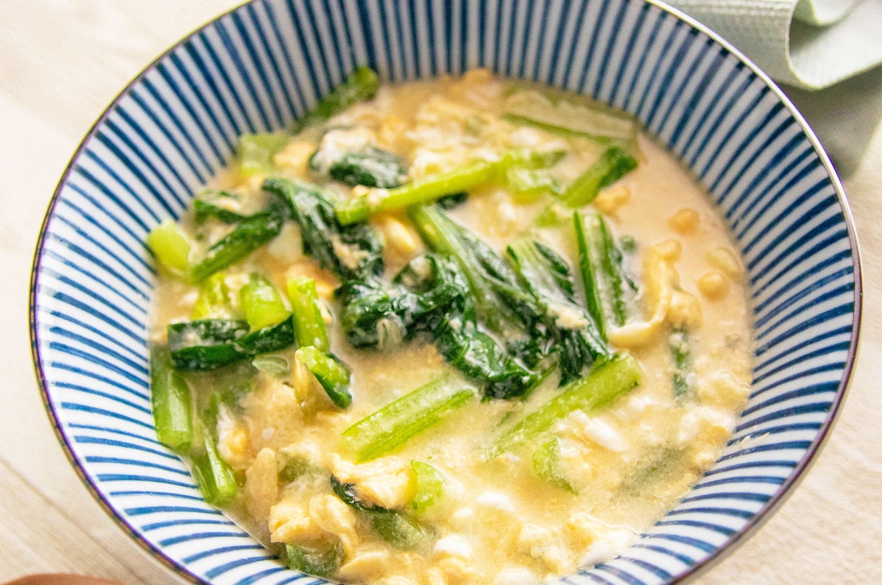 ボウルに入ったクリーミーソースをかけた野菜と豆類の料理。テーブルには木のスプーンが置かれています。