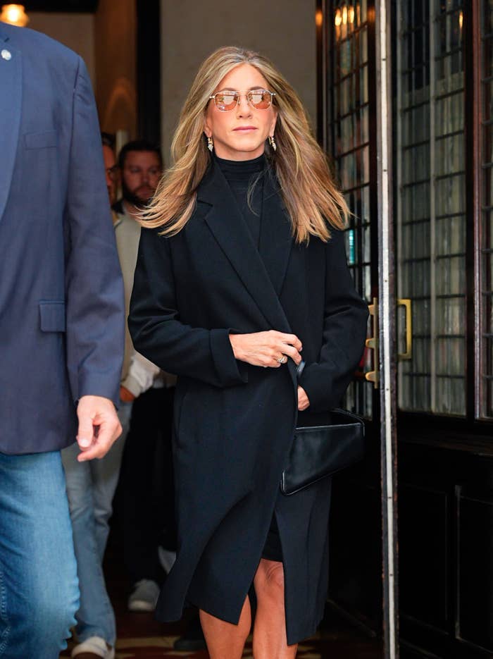 Jennifer Aniston in a black coat and sunglasses walking outside