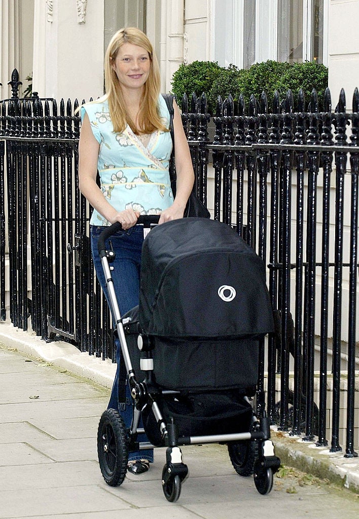21 Low-Key Ridiculous Things Celebs Did For Money, Clout, Or Attention 46 A woman with long blonde hair, wearing a floral top and jeans, is pushing a black stroller on a city sidewalk. She appears content and relaxed.