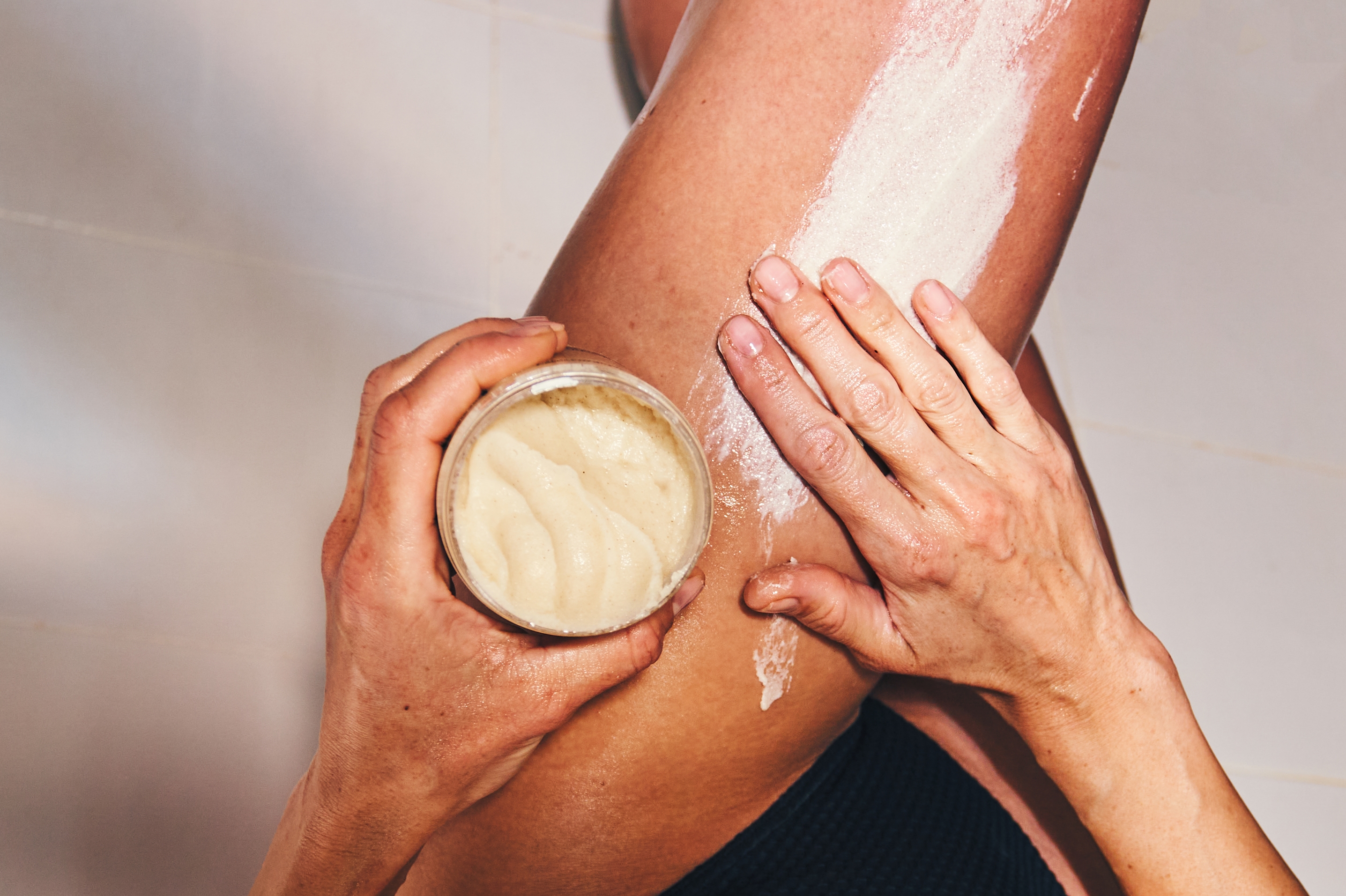 A person applies body scrub to their leg using their hands, emphasizing self-care and skincare ritual