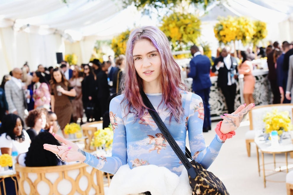 21 Low-Key Ridiculous Things Celebs Did For Money, Clout, Or Attention 8 Grimes with colorful hair in a fitted, cherub-print top at an event with floral decor in the background