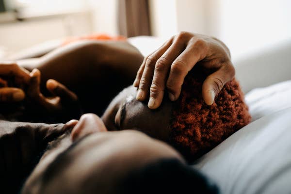Two people lie close together in an intimate moment, one gently cradling the other&#x27;s head, capturing a sense of affection and connection
