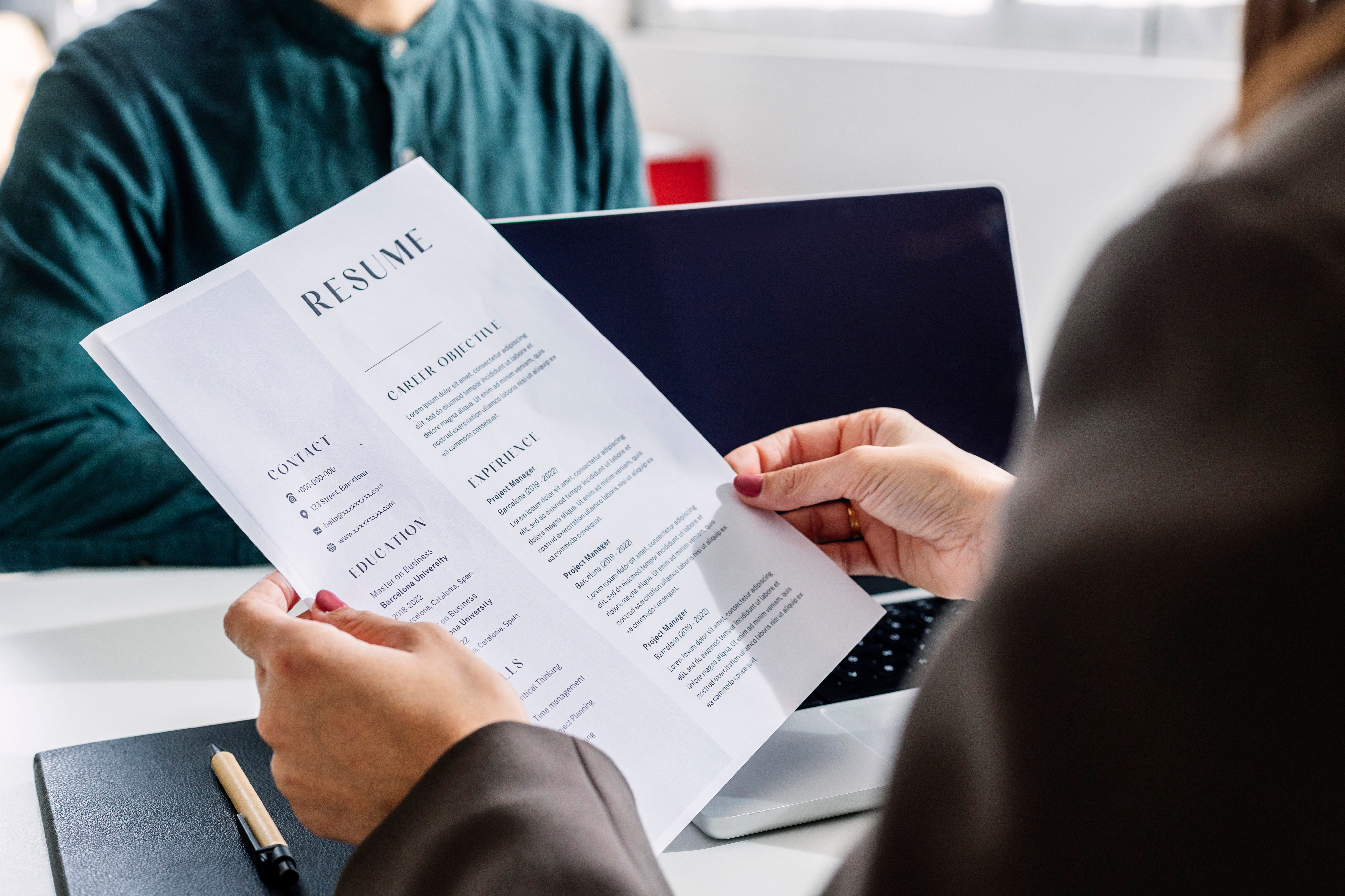 Person reviewing a detailed resume in an office setting, with a laptop in the background. Focus on job experience and skills