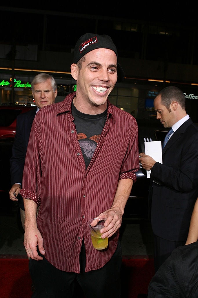 21 Low-Key Ridiculous Things Celebs Did For Money, Clout, Or Attention 32 Steve-O at a red carpet event wearing a striped shirt, casual hat, and holding a drink