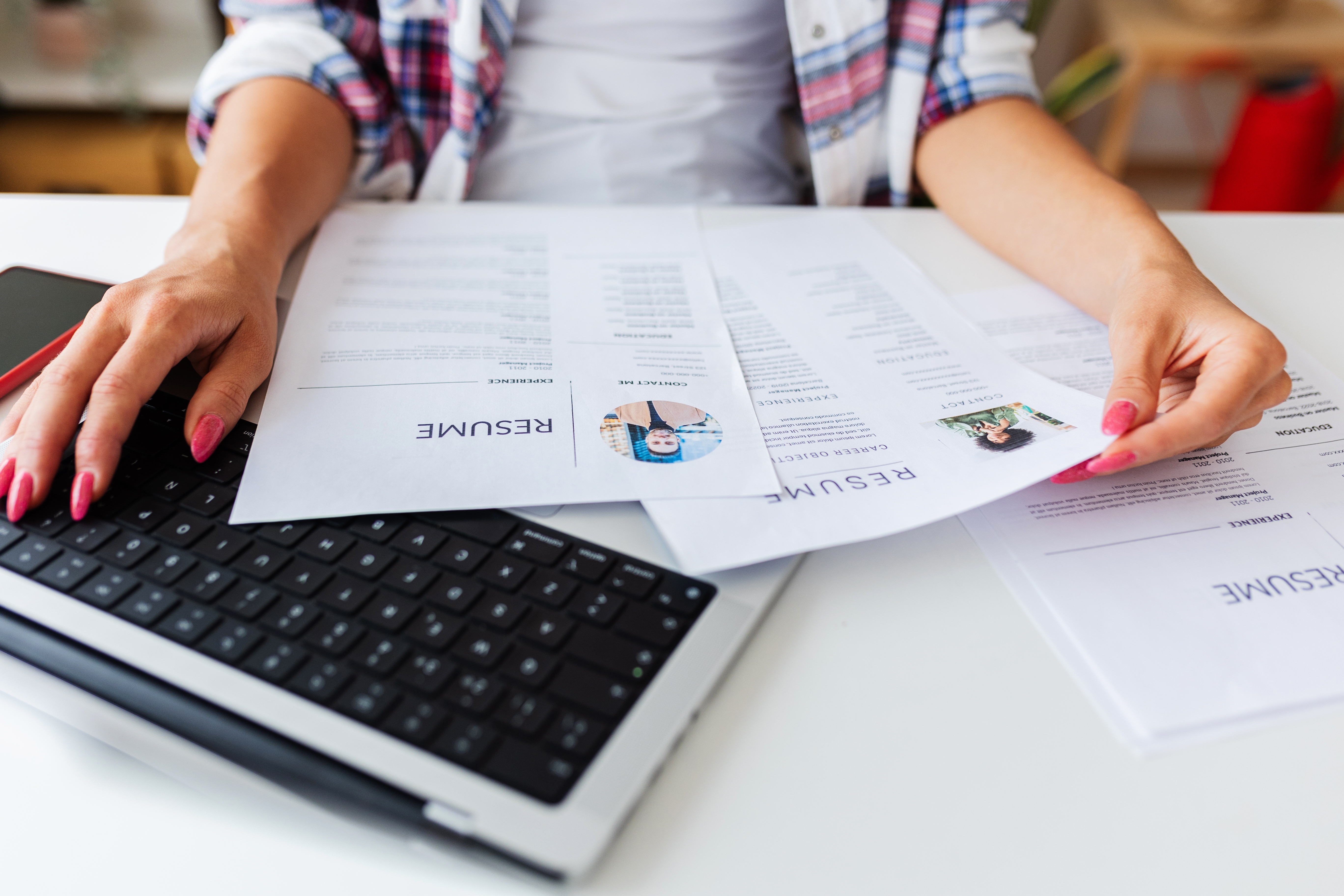 Person reviewing printed resumes on a laptop keyboard, focusing on career details