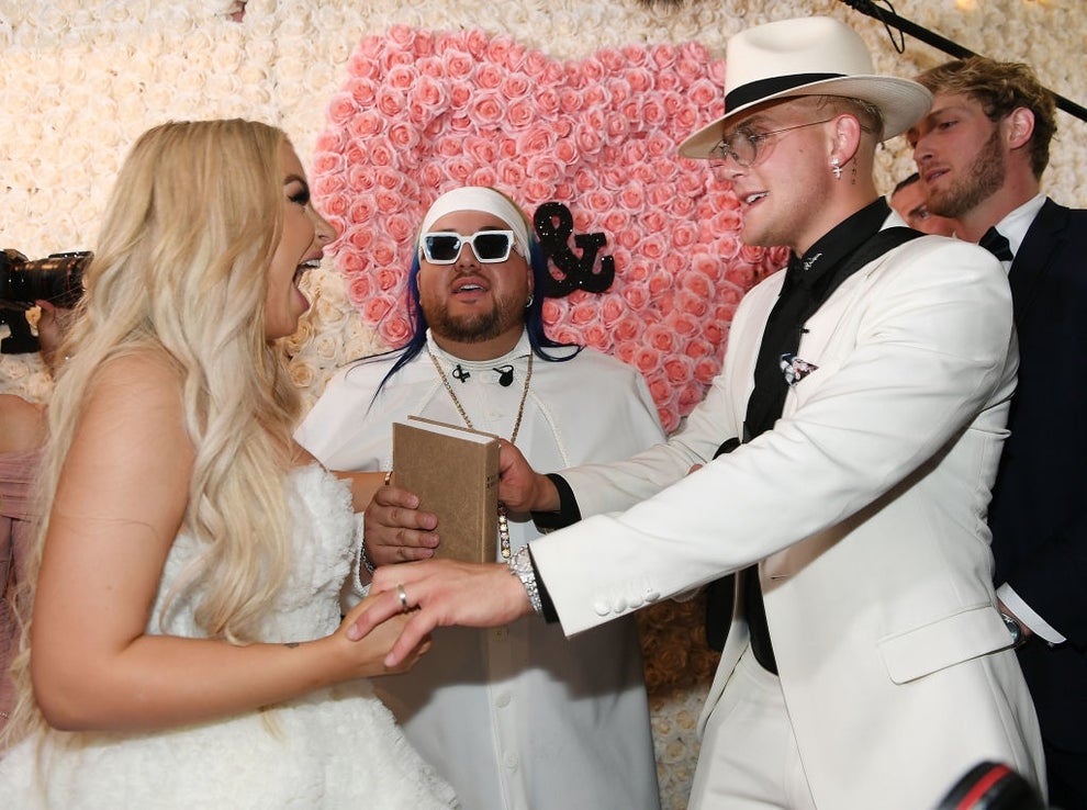 21 Low-Key Ridiculous Things Celebs Did For Money, Clout, Or Attention 66 A joyful moment at a lively wedding ceremony; a couple in white outfits hold hands, surrounded by guests. Pink floral backdrop adds a festive touch.