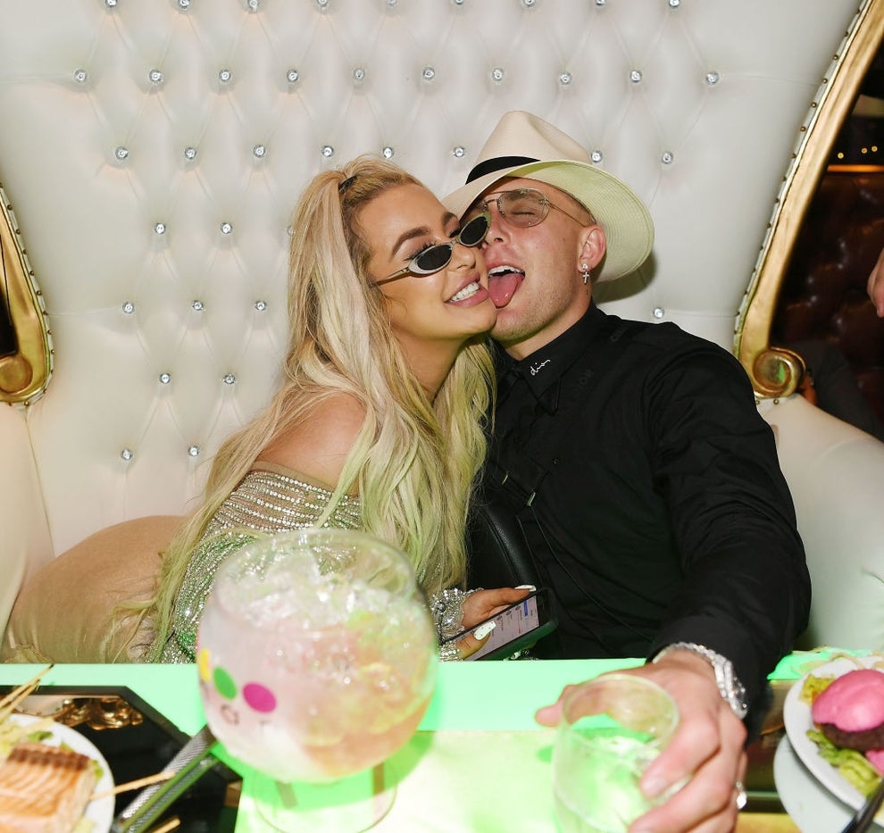 21 Low-Key Ridiculous Things Celebs Did For Money, Clout, Or Attention 68 A couple smiling and posing playfully in an opulent setting. One is wearing a hat, and the other has sunglasses. They appear joyful and relaxed.