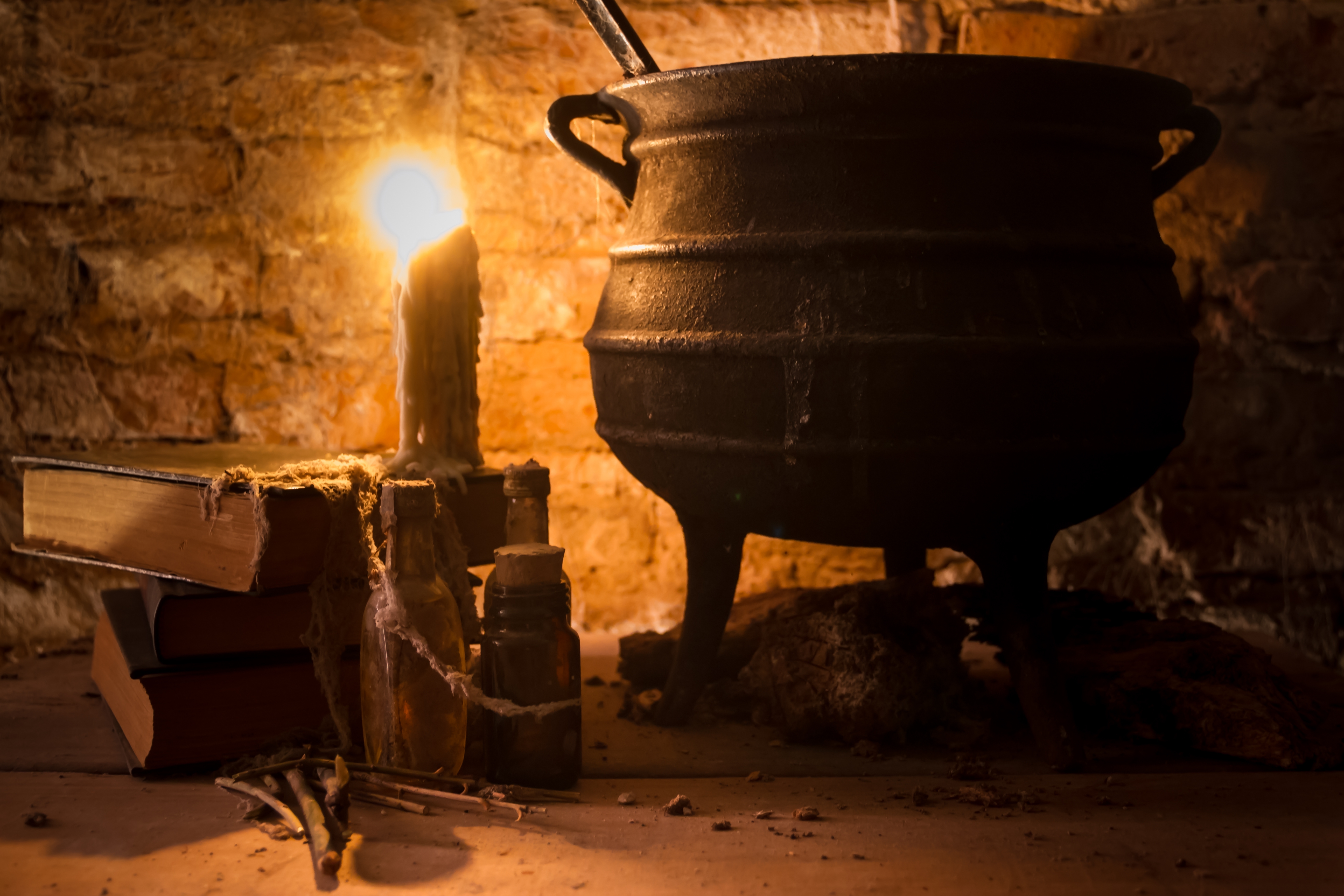 En rustikk gryte i et svakt opplyst rom med et gammelt lys som brenner ved siden av stablede bøker og drikkeflasker, og skaper en mystisk scene