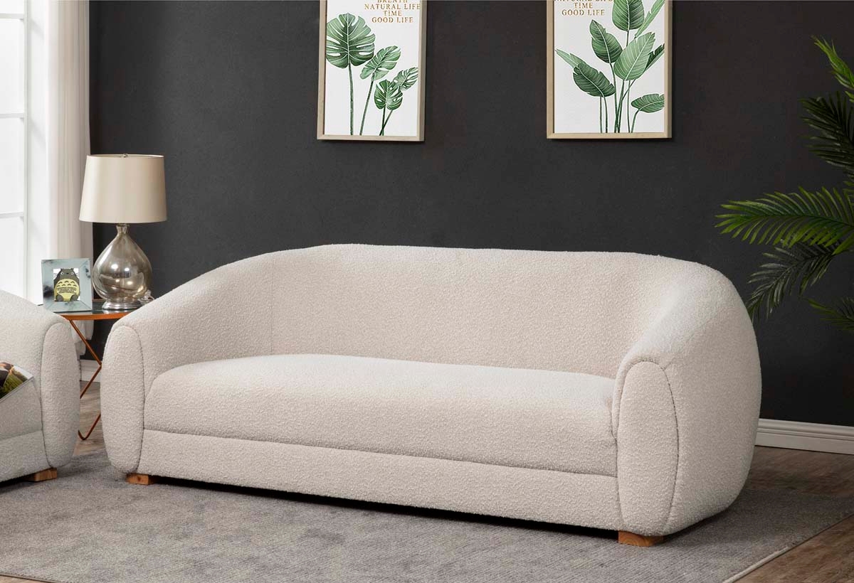 Modern, curved sofa with a soft, textured fabric in a living room. Two plant-themed pictures and a lamp are in the background