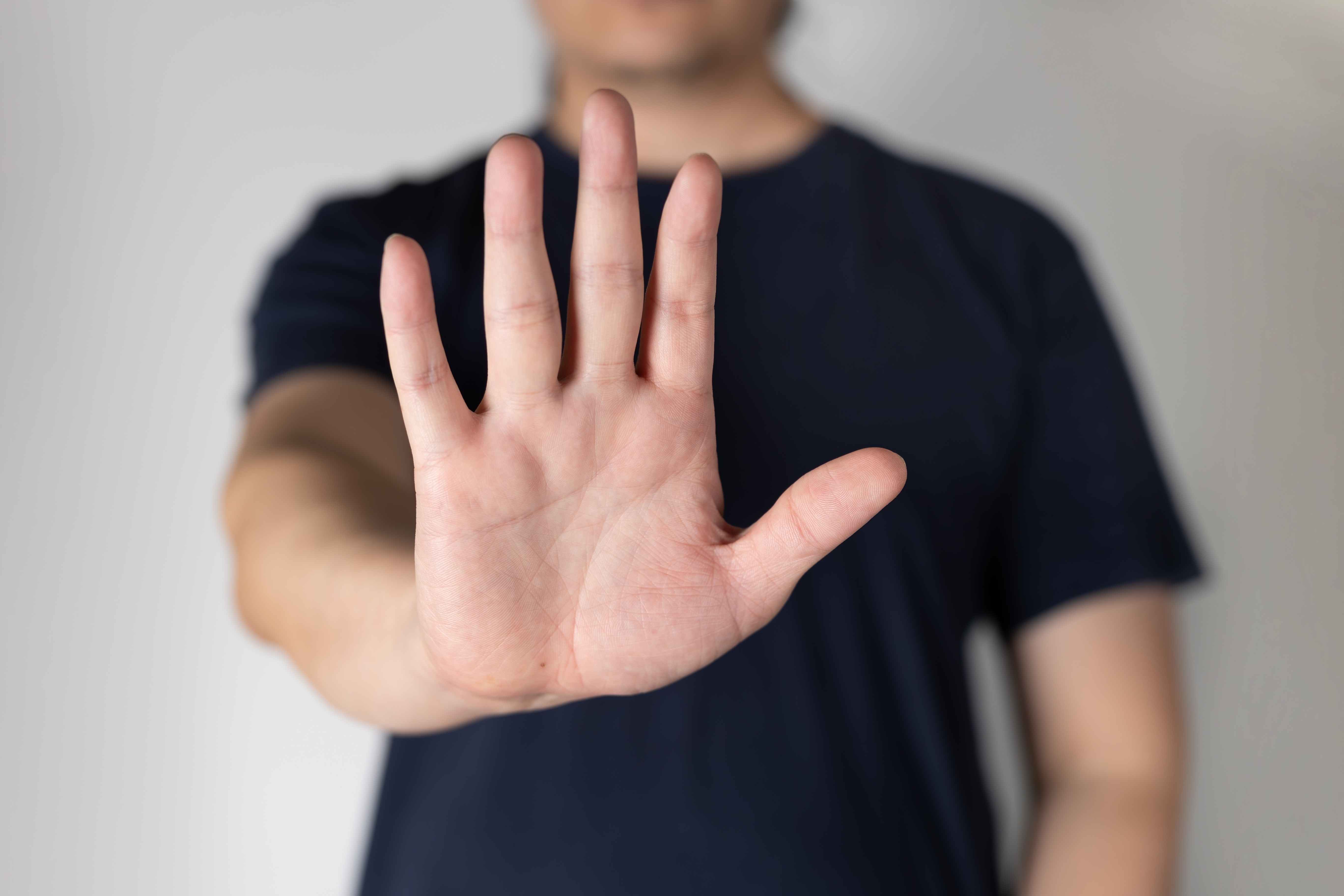 Person som strekker ut en åpen hånd mot kameraet, med håndflaten vendt fremover, i en gest som vanligvis forbindes med å stoppe eller si