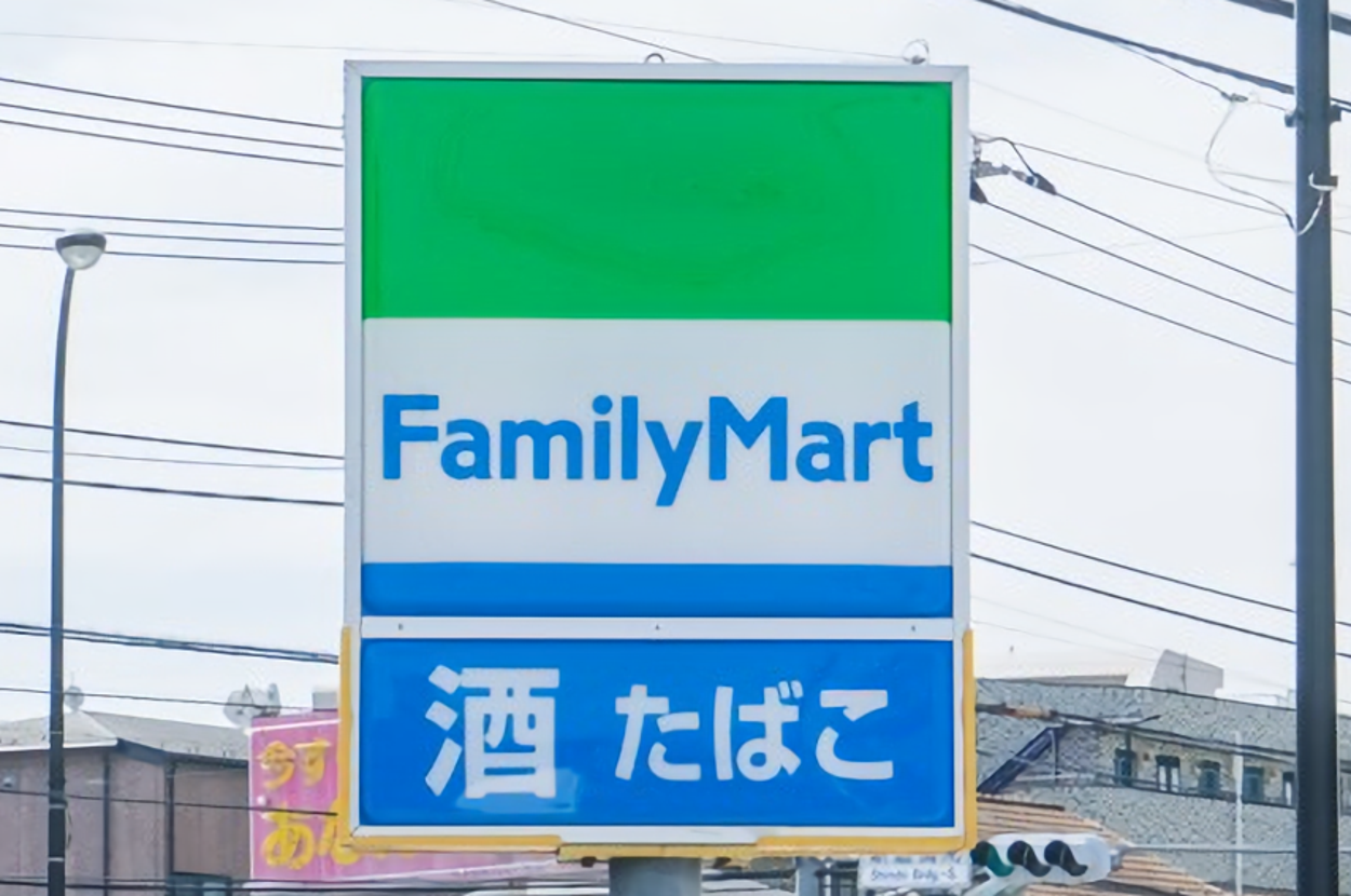 ファミリーマートの看板。「酒」「たばこ」と表示されています。背景に電柱や建物が見えます。