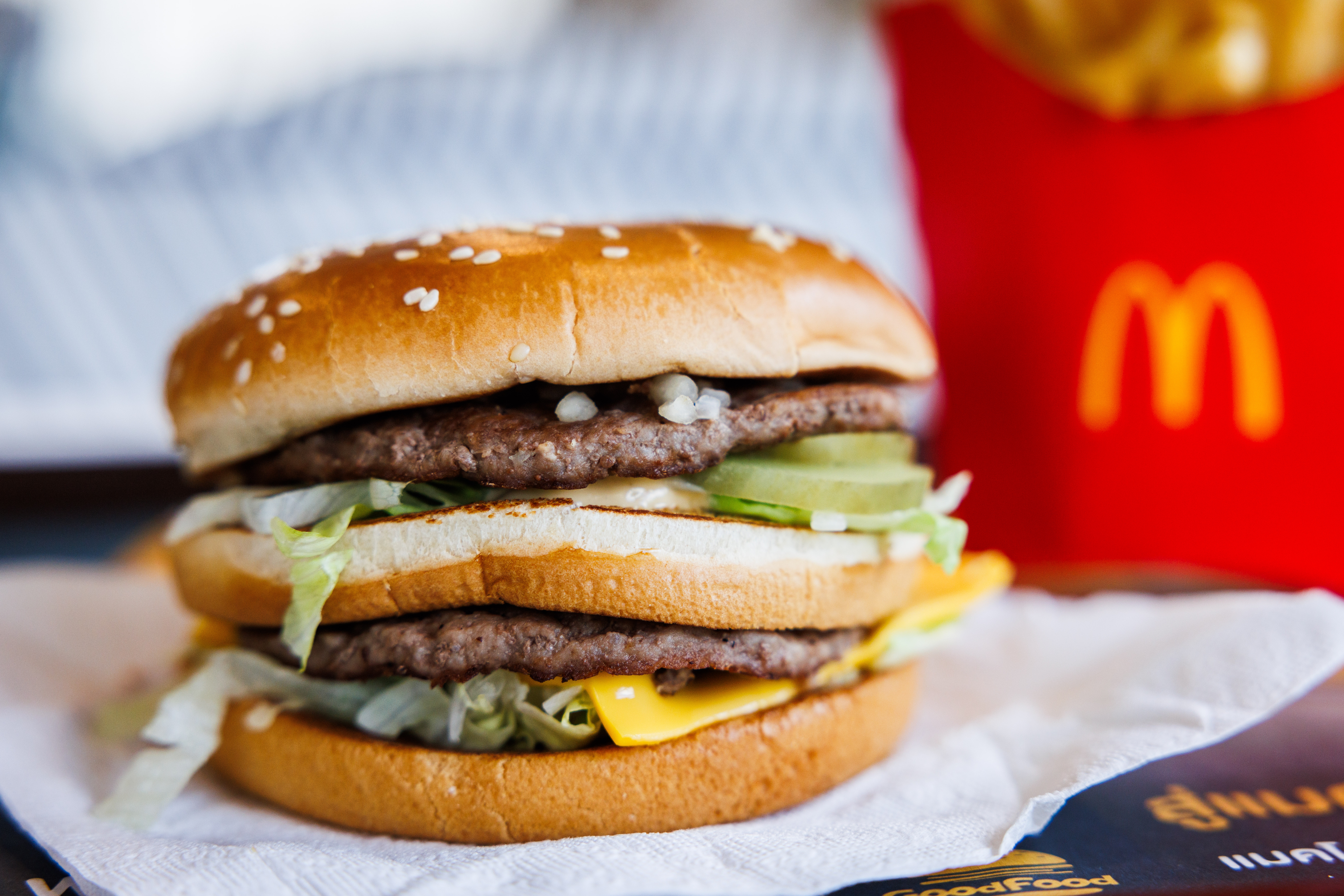 Close-up of a McDonald's Big Mac with two beef patties, cheese, lettuce, pickles, onions, and special sauce, next to a container of fries