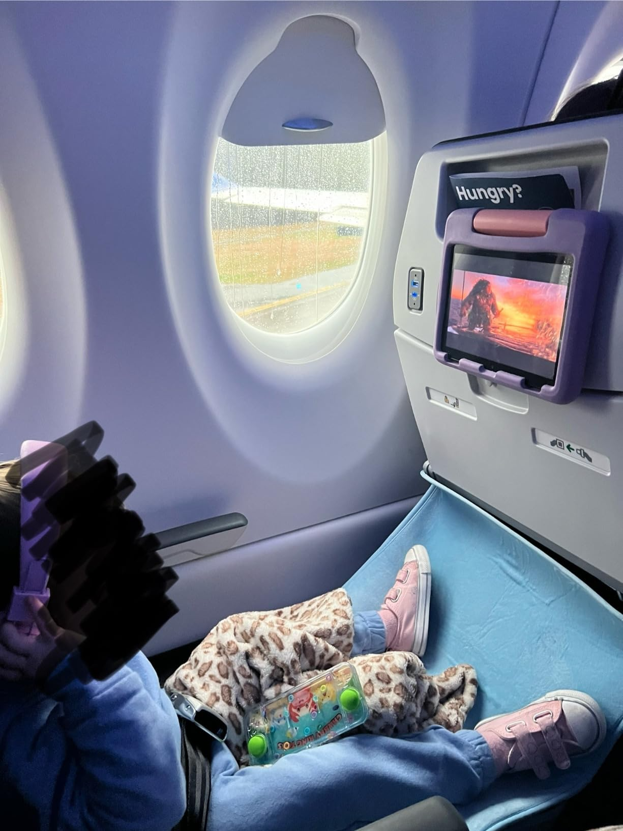 Child reclines connected  airplane spot   with artifact  and surface  showing cartoon. Pink shoes and leopard broad  visible. The tray array  displays 
