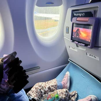 Child reclines connected airplane spot with artifact and surface showing cartoon. Pink shoes and leopard broad visible. The tray array displays