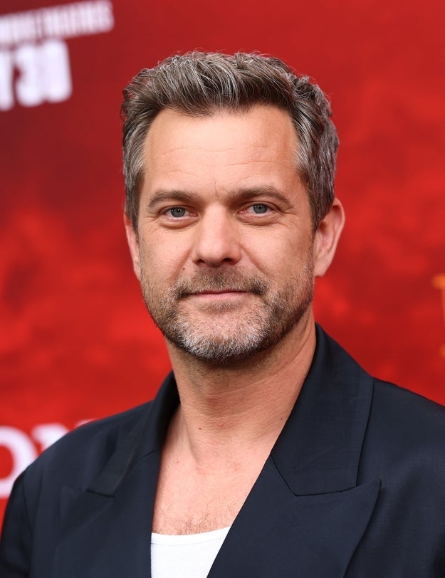 21 Jaw-Dropping "Then And Now" Photos Of Celebrities Who Have Gotten Wayyyyy Sexier With Age 10 Person in a dark jacket and white shirt at a red carpet event, posing for the camera