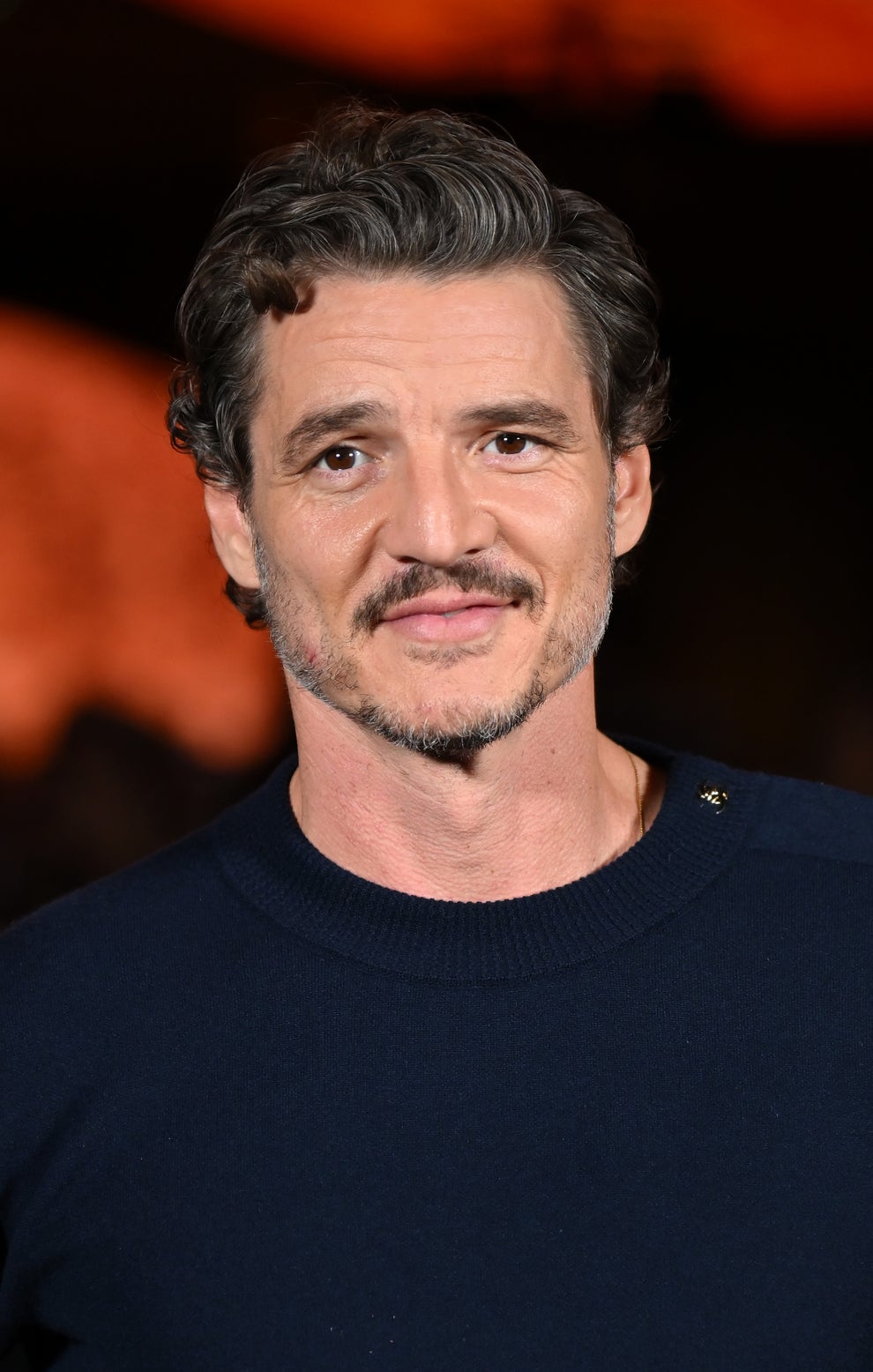 21 Jaw-Dropping "Then And Now" Photos Of Celebrities Who Have Gotten Wayyyyy Sexier With Age 30 Person posing at an event, wearing a casual, plain long-sleeved shirt, smiling at the camera